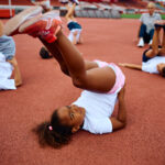 Our Projects African American girl and her friends warming up while having exercise class at the stadium. She is looking at camera.